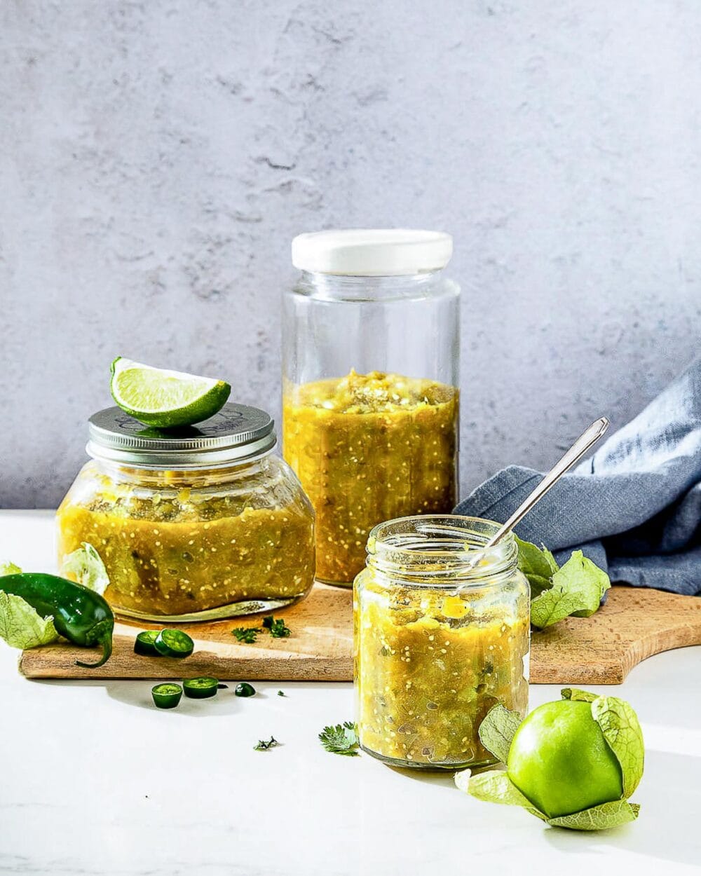 salsa verde in glass jars, tomatillos sitting next to the jars.