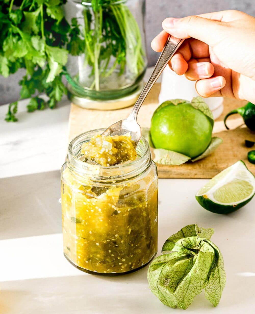 spooning tomatillo salsa verde out of a glass jar.