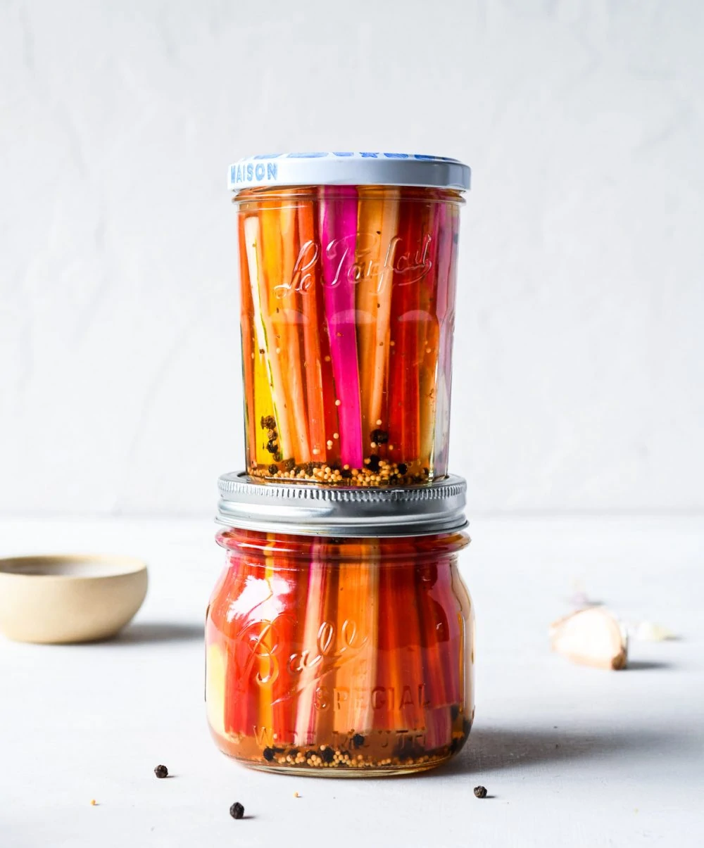pickled chard stems in two glass jars with lids, stacked on top of each other