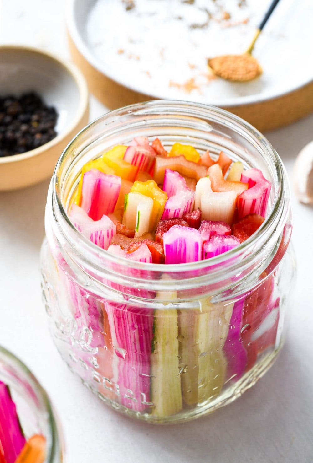 swiss chard stems in a clear jar, with peppercorns and spices in the backround