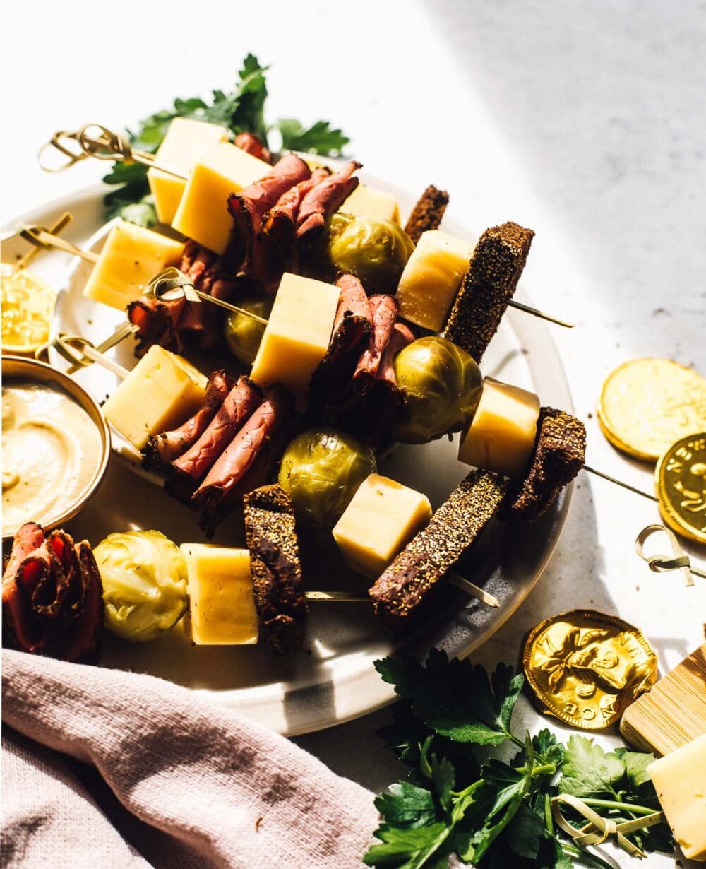skewers with pastrami, pickled brussels sprouts, cheese, rye bread on a white plate