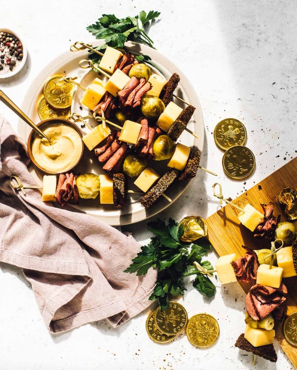 irish skewers on a white plate, with pastrami and pickled brussels sprouts, cheese. pink napkin to the left of plate, gold chocolate coins to the right of plate. 
