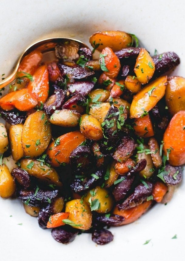 caramelized carrots in a white bowl with a gold spoon. 