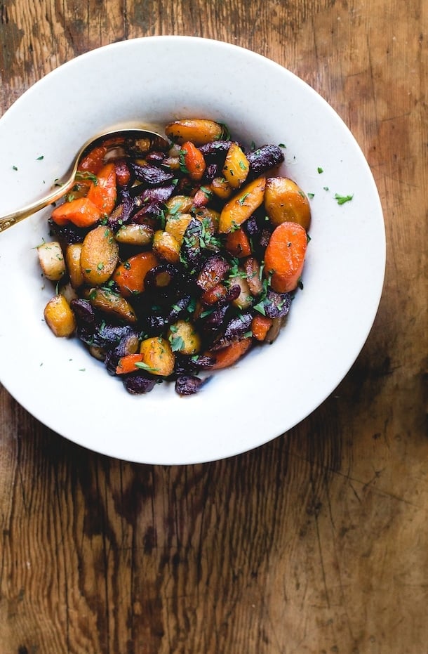 Caramelized Honey Garlic Carrots in a white bowl, with gold spoon, sitting on a wooden table. 