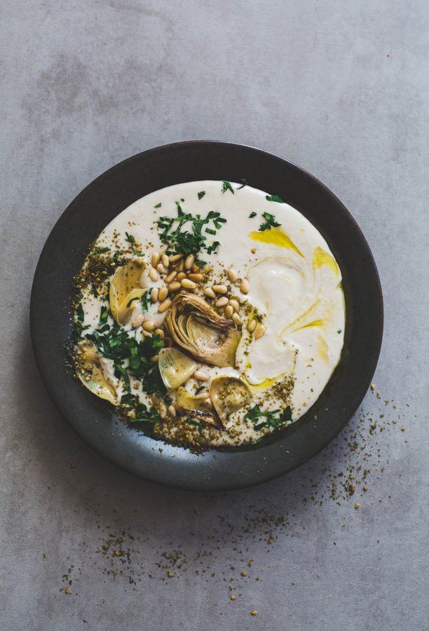a plate of Silky White Bean Hummus with Artichokes and Pine Nuts in a black bowl