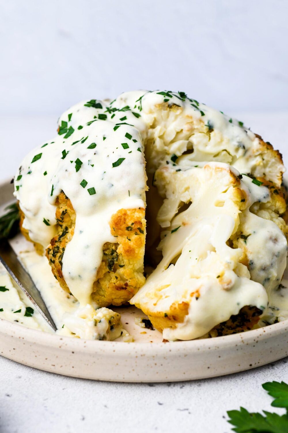 whole roasted cauliflower on a plate with cheese sauce