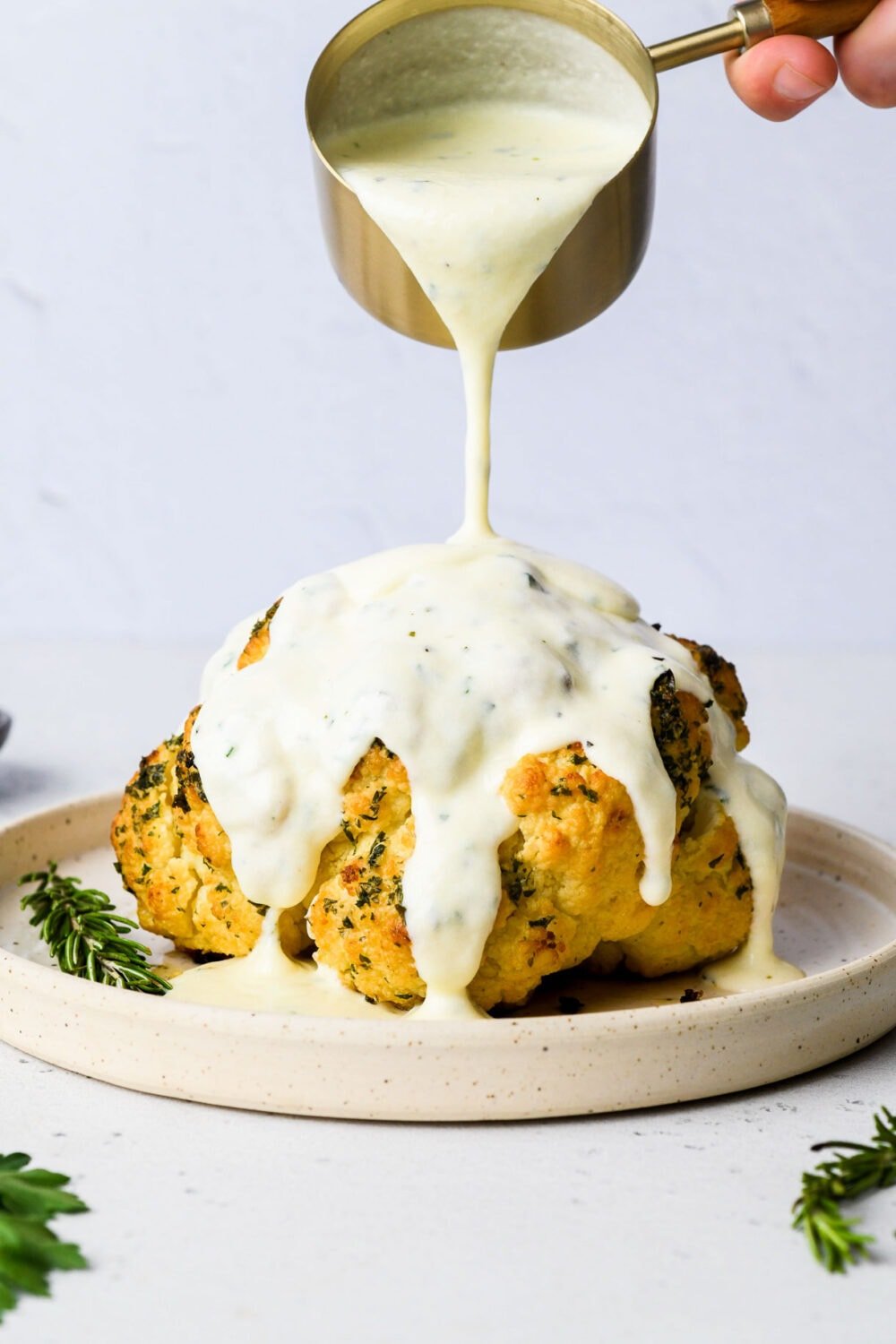 pouring cheese sauce over roasted cauliflower