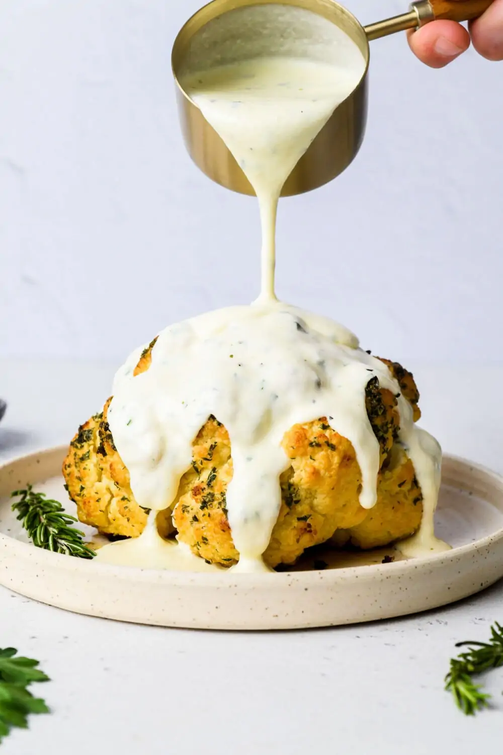pouring cheese sauce over roasted cauliflower