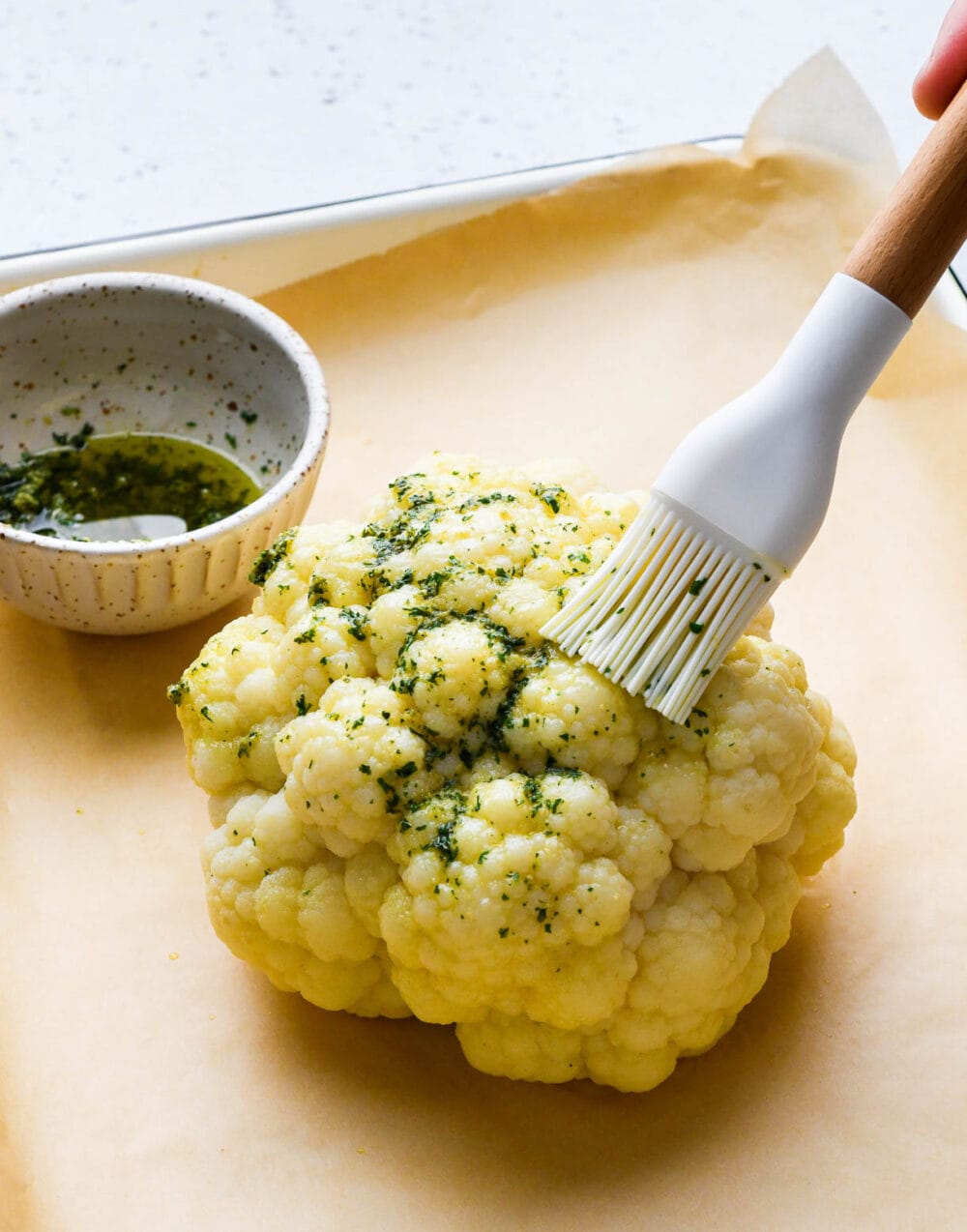 brushing raw cauliflower with olive oil and herbs