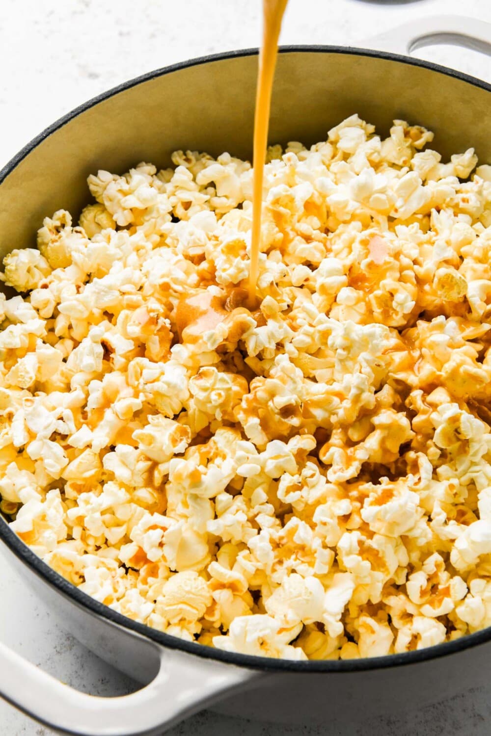 pouring caramel over popcorn in a dutch oven