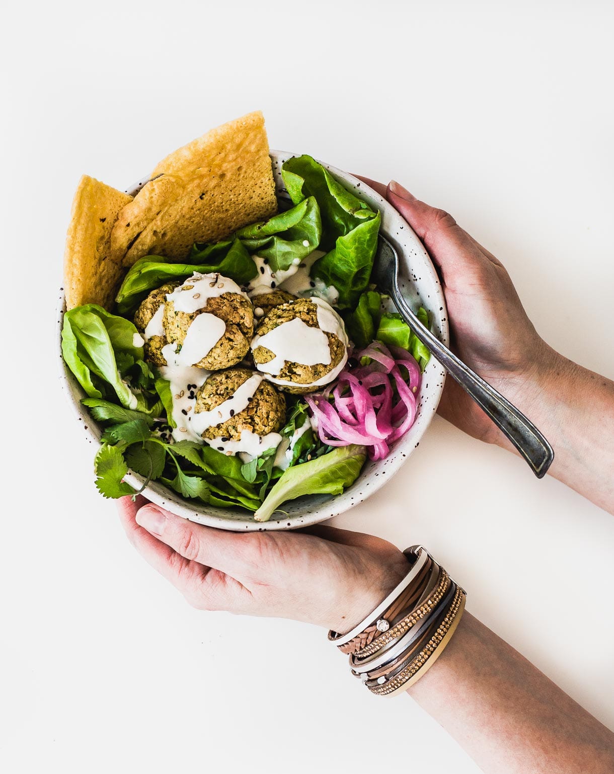 Bowl of salad topped with baked falafel, held in someone's hands, overhead angle.