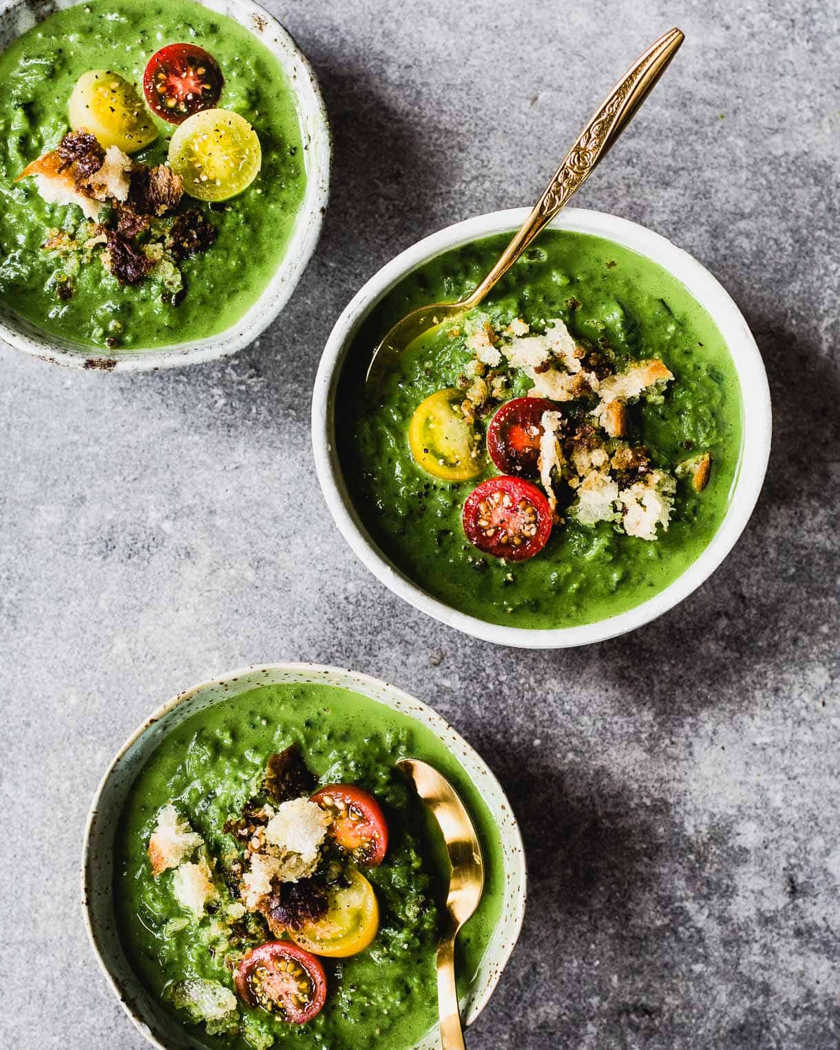 three bowls of broccoli soup with gold spoons