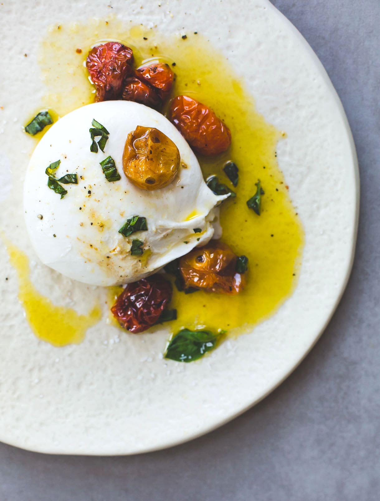 burrata cheese on plate with roasted cherry tomatoes and basil