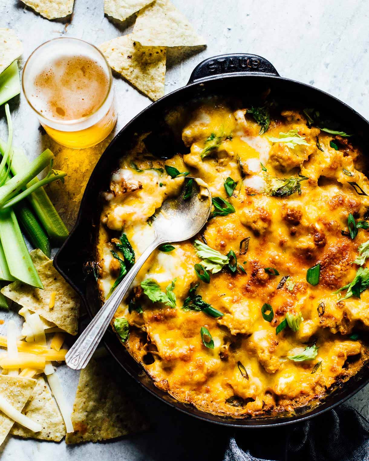 Buffalo Cauliflower Dip in a cast iron skillet, with glass of beer next to it