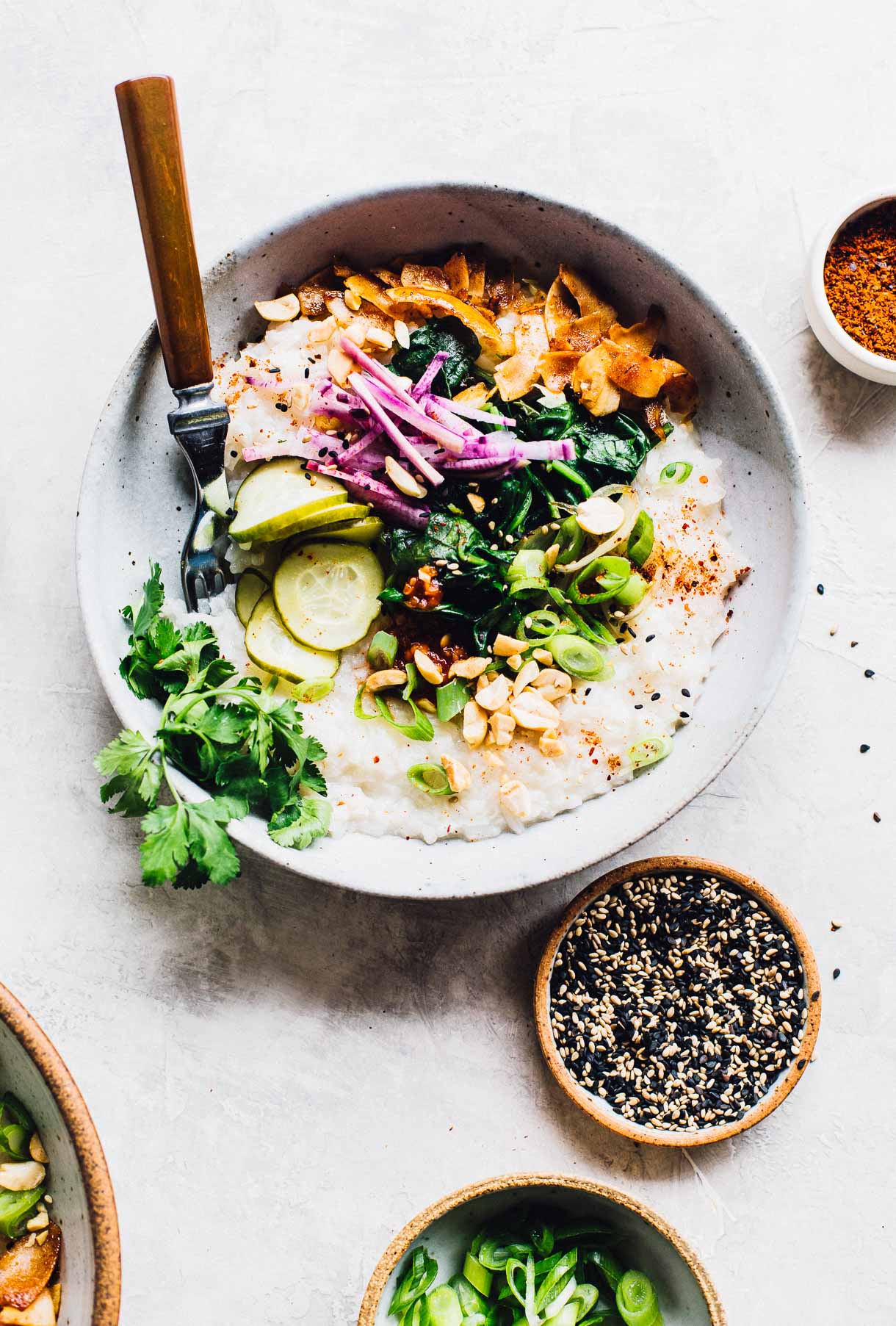 instant pot congee in a bowl with spinach, coconut, pickles, green onions, peanuts