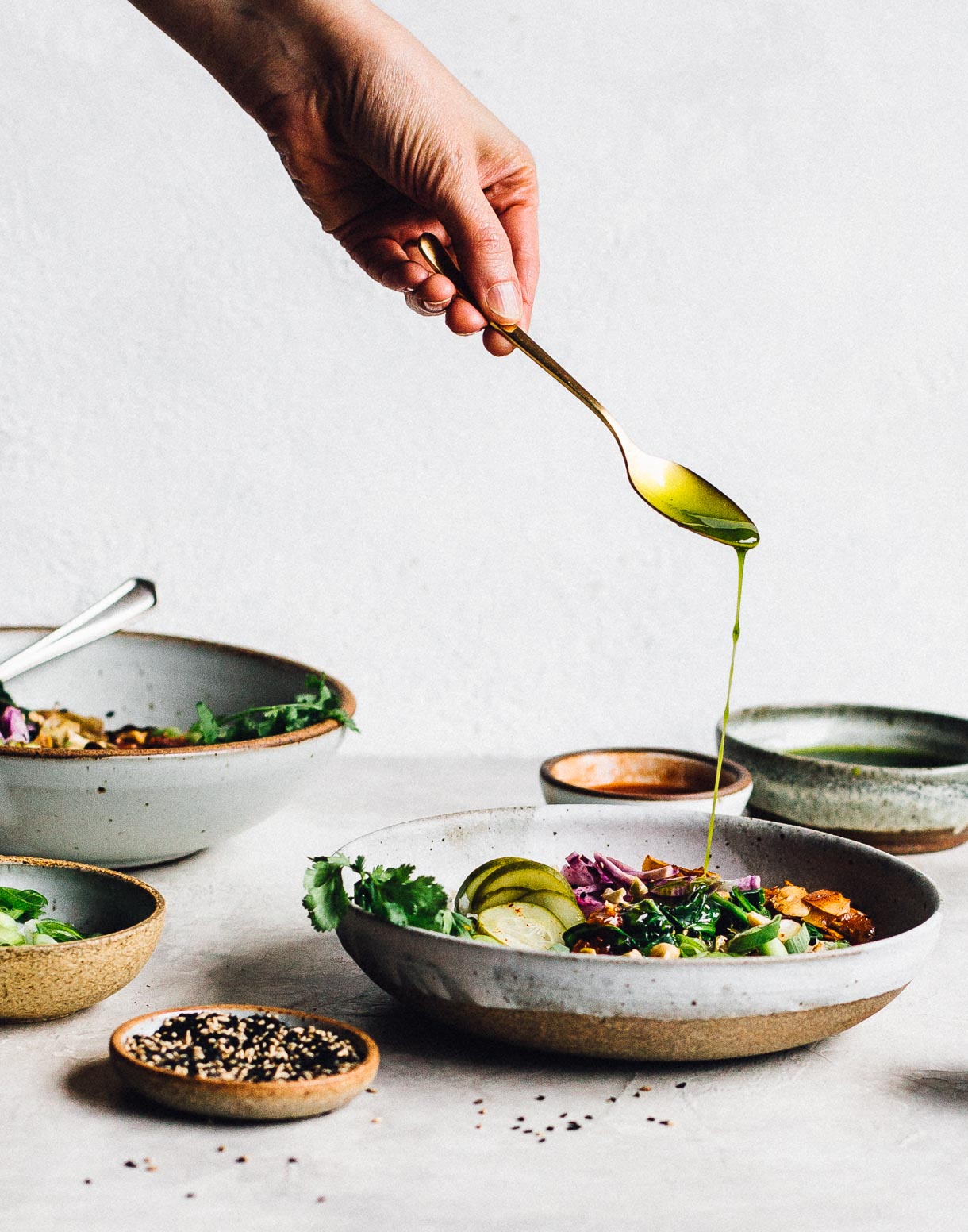 Drizzling cilantro oil on congee rice bowls, with sesame seeds in foreground. 