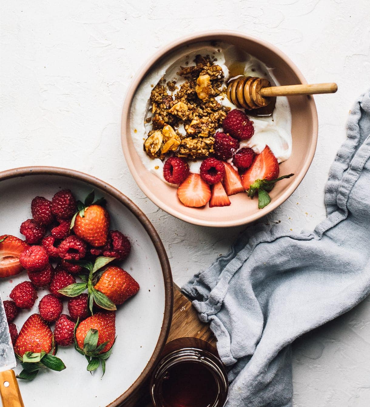 bowl of yogurt topped with granola and bowl of raspberries and strawberries