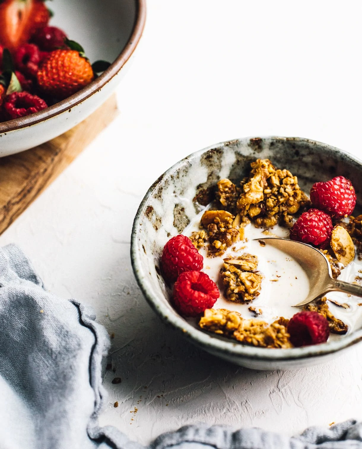 bowl of granola and milk, with bowl of raspberries in backround