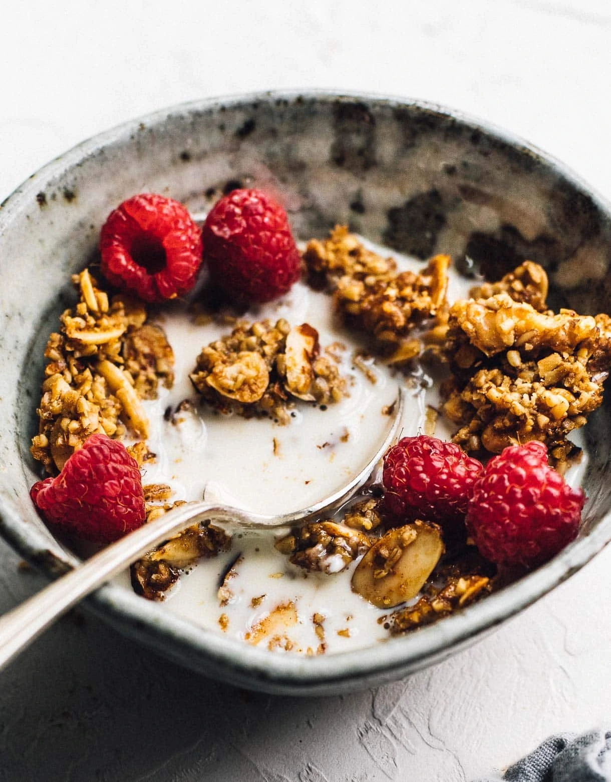 extra clumpy granola in a bowl with milk and raspberries