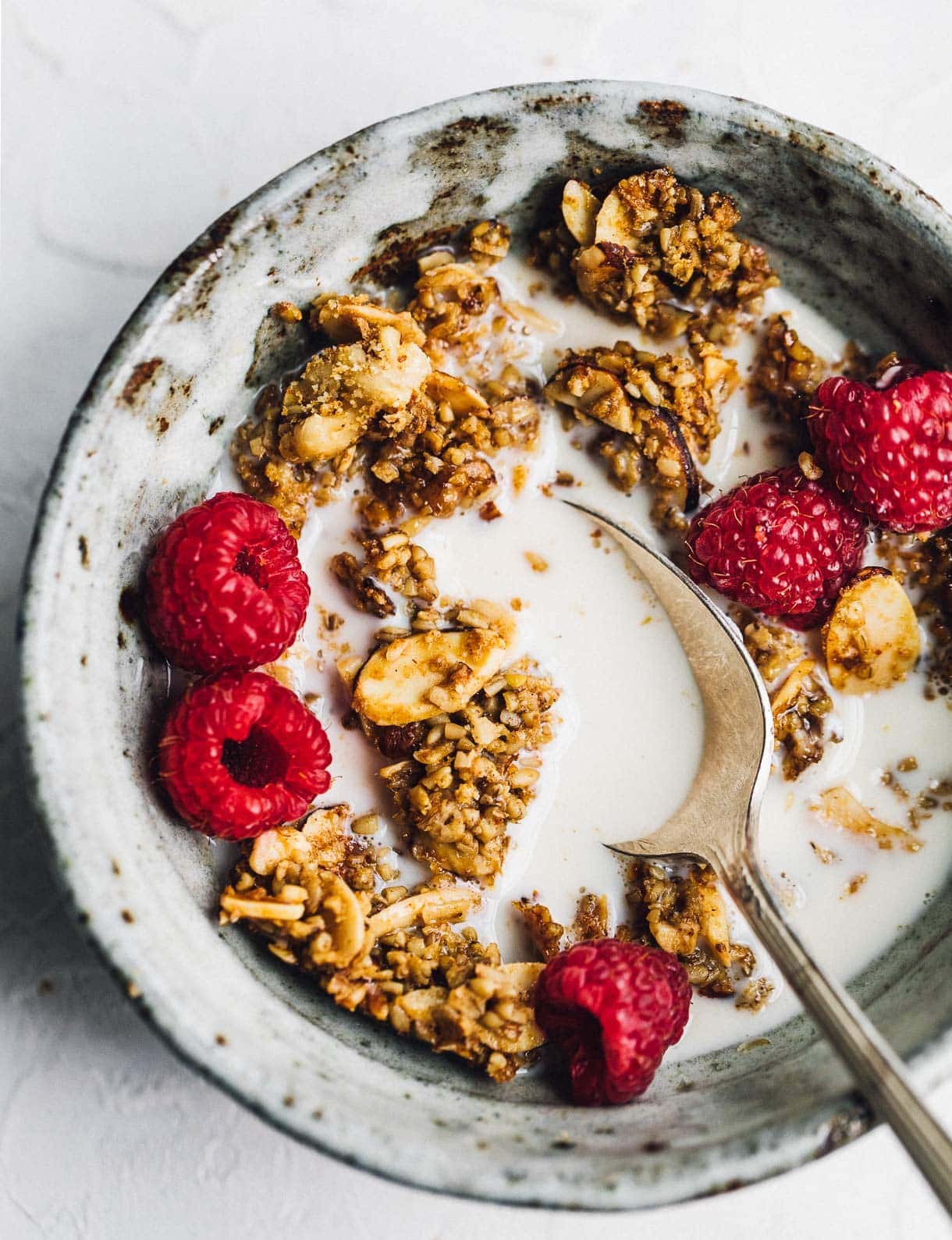 extra clumpy granola in a bowl with milk and raspberries