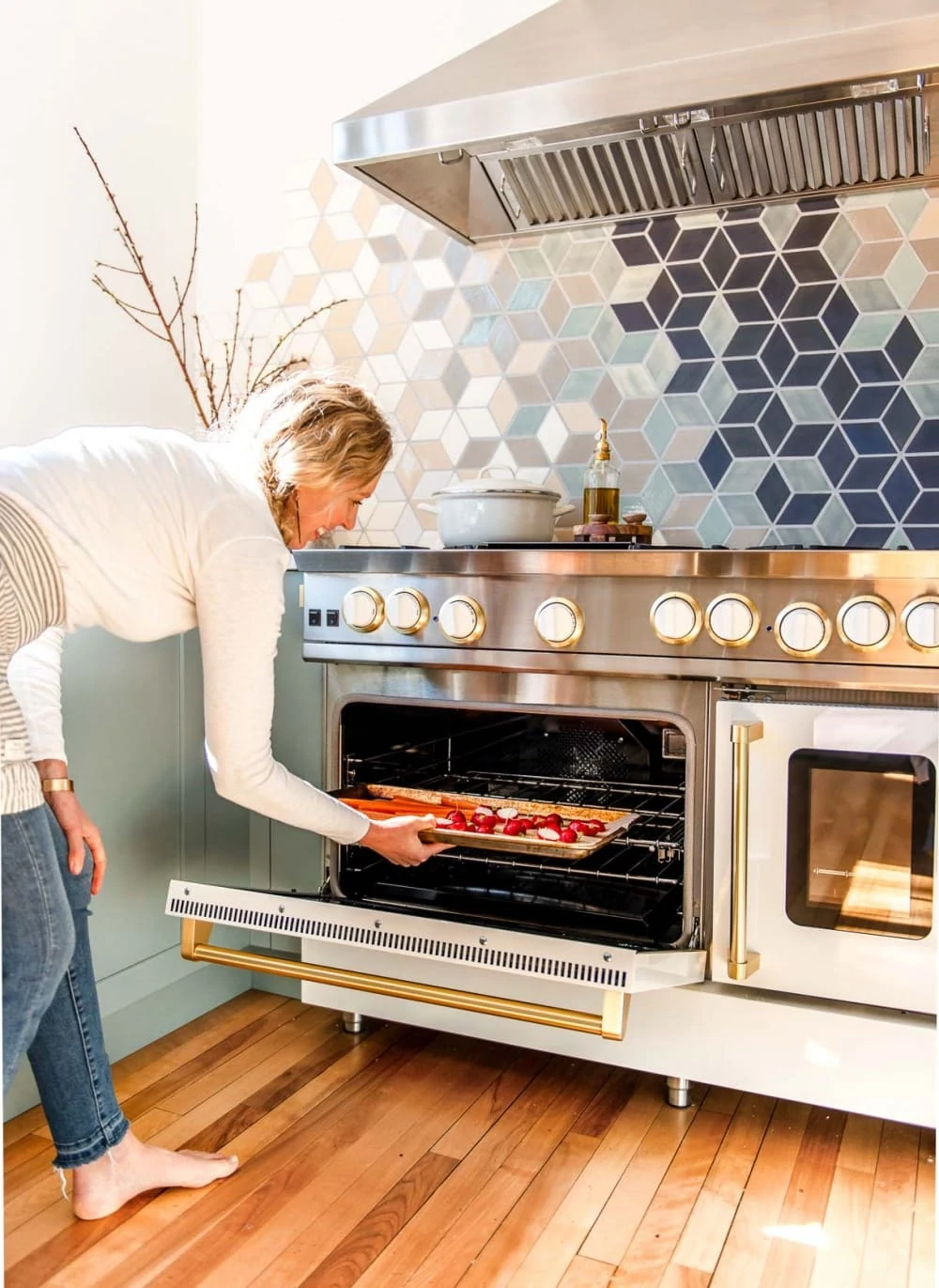 woman putting sheet pan of carrots and radishes into a white blue star oven