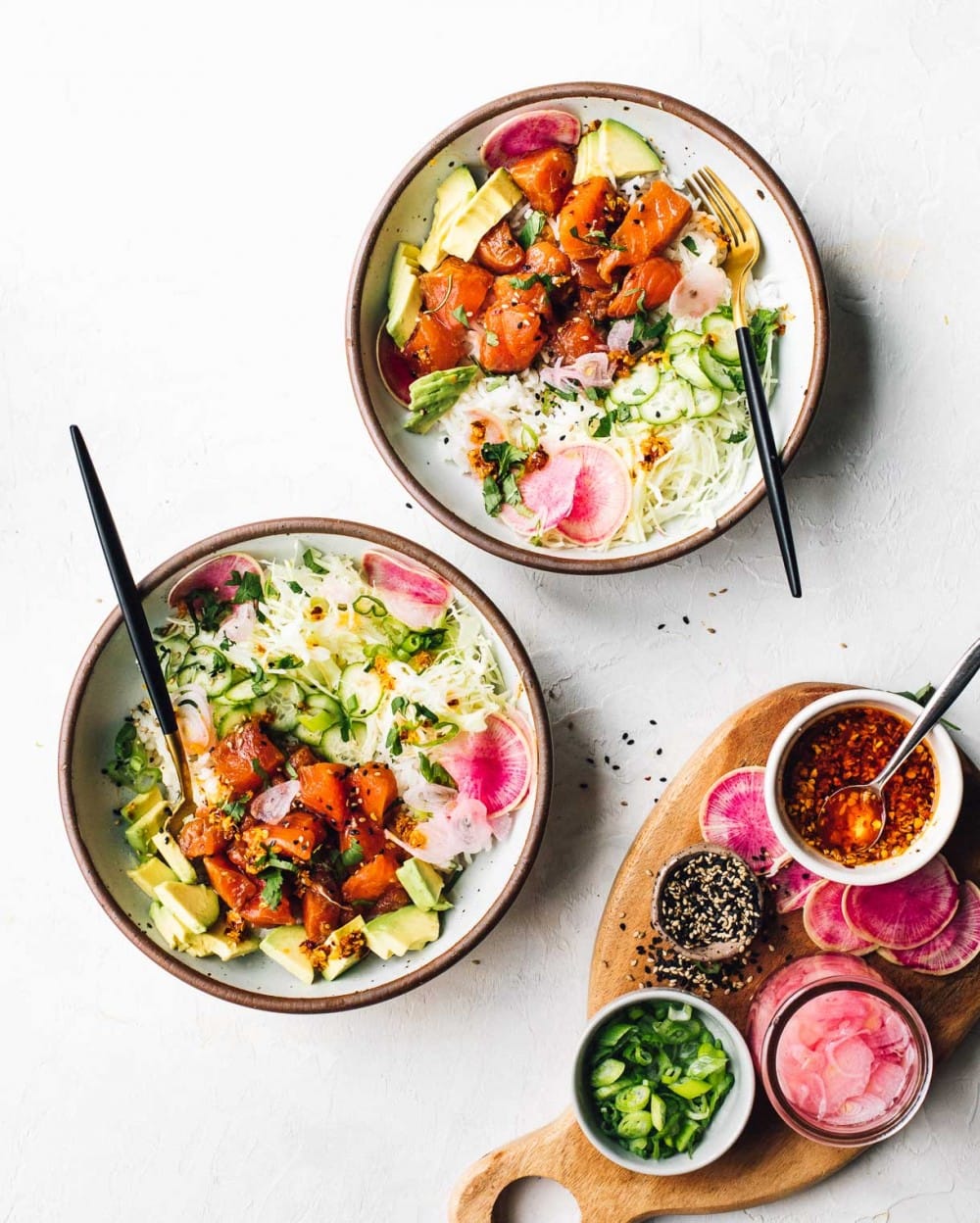 two bowls of salmon poke with a cutting board to the side that has condiments