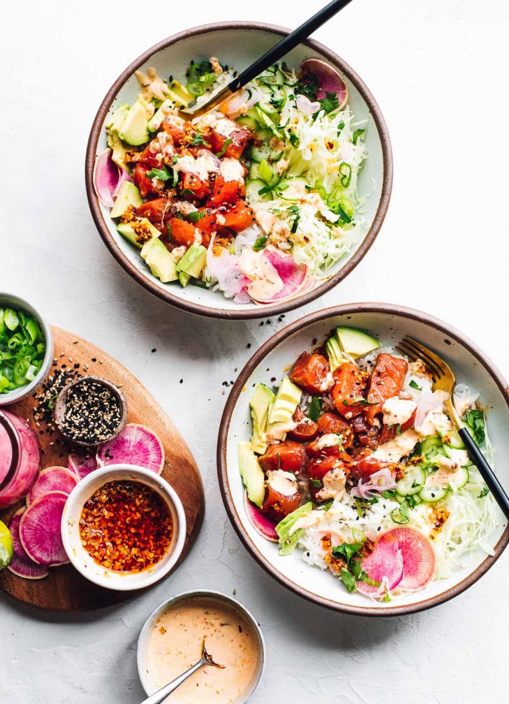 two bowls of salmon poke with a cutting board to the side that has condiments