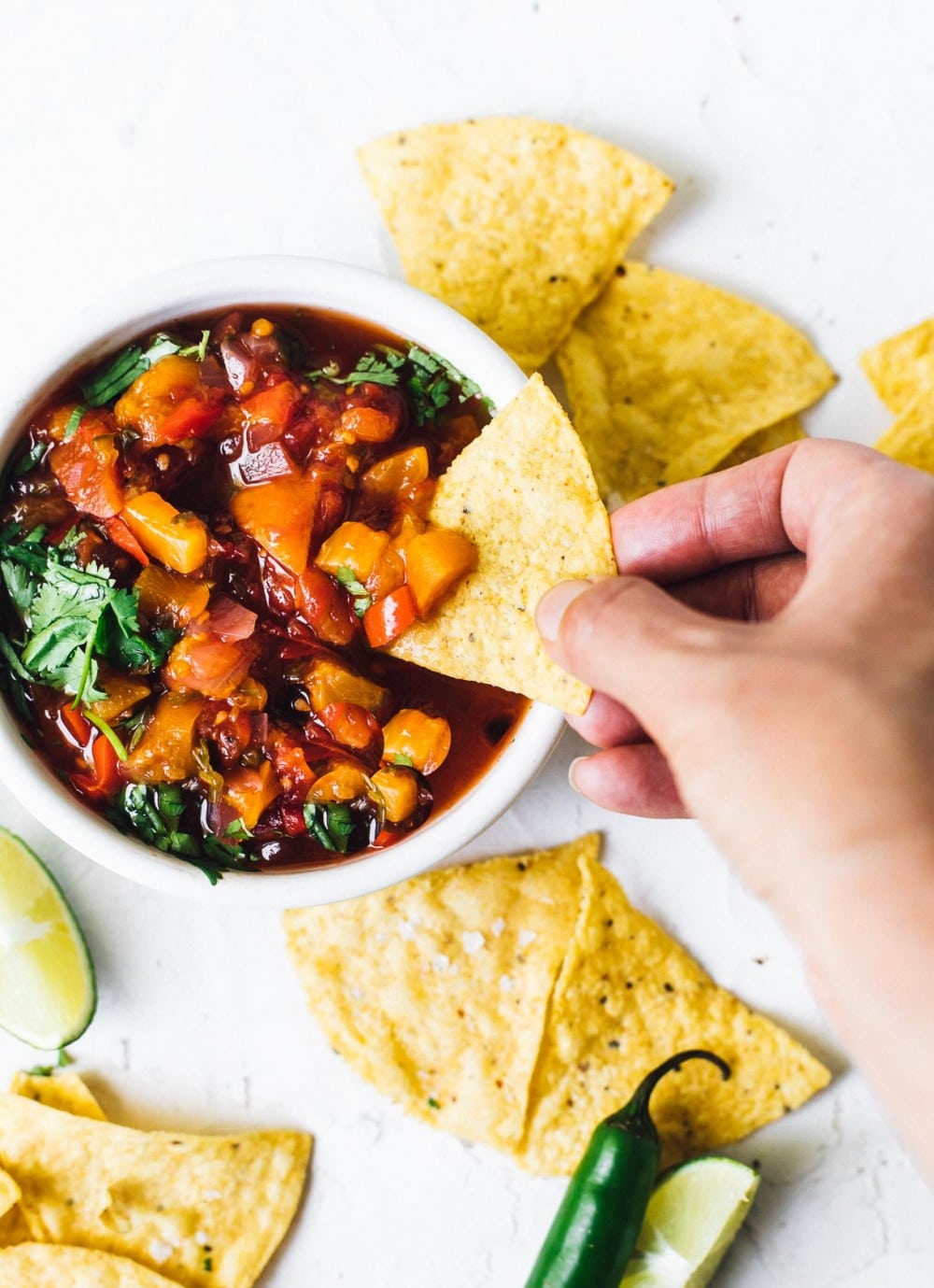 dipping a tortilla chip into tomato peach salsa