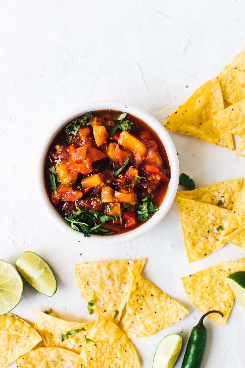tomato peach salsa in a bowl with chips around it, and limes