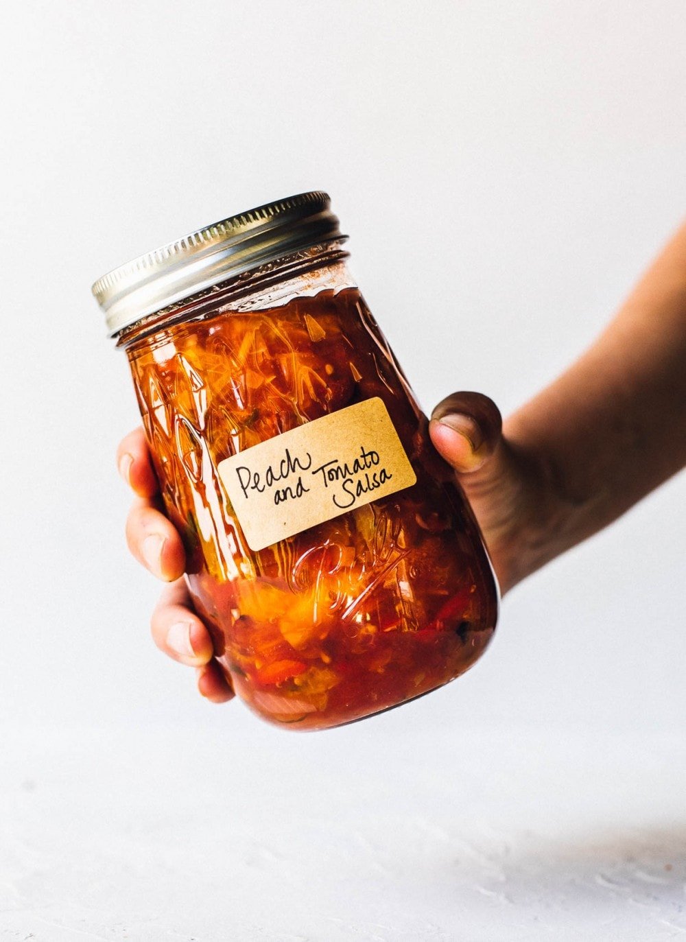 holding a jar of tomato peach salsa