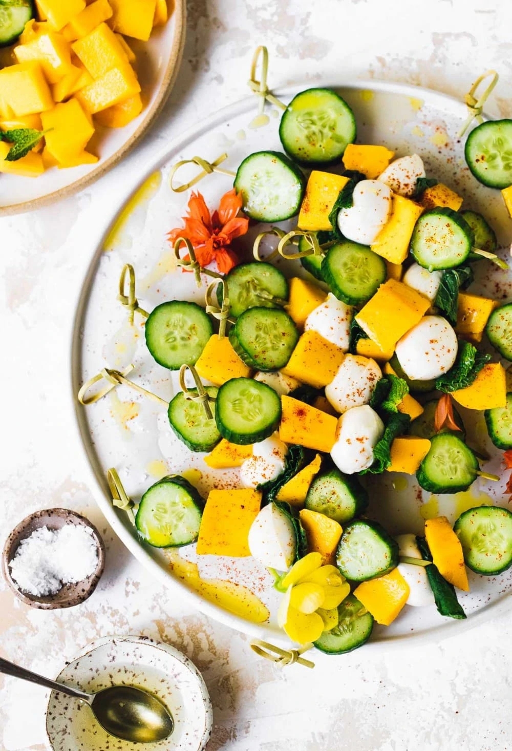 mango mozzarella cucumber skewers on a plate, with bowl of salt and white balsamic vinegar next to it