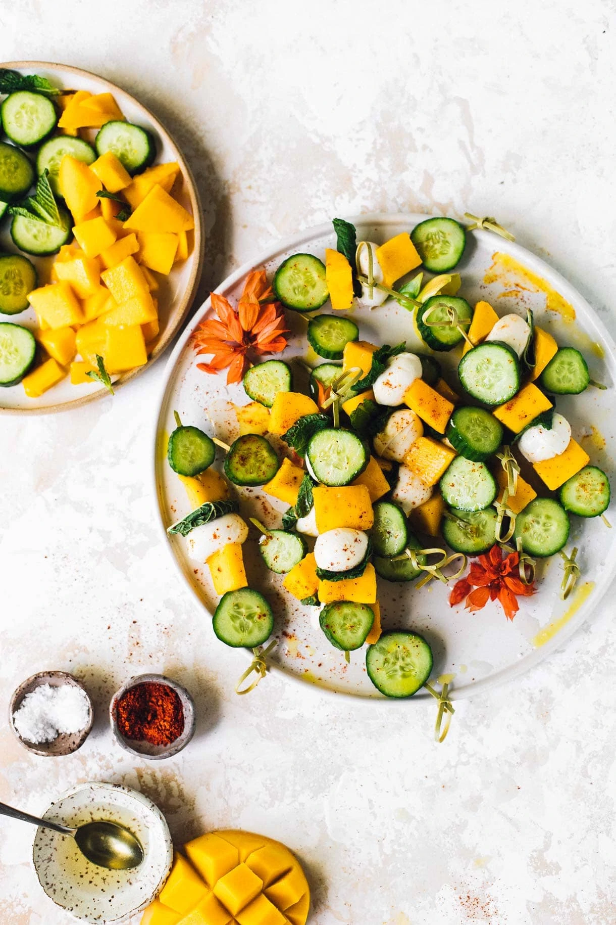 mango mozzarella cucumber skewers on a plate, with bowl of salt and white balsamic vinegar next to it