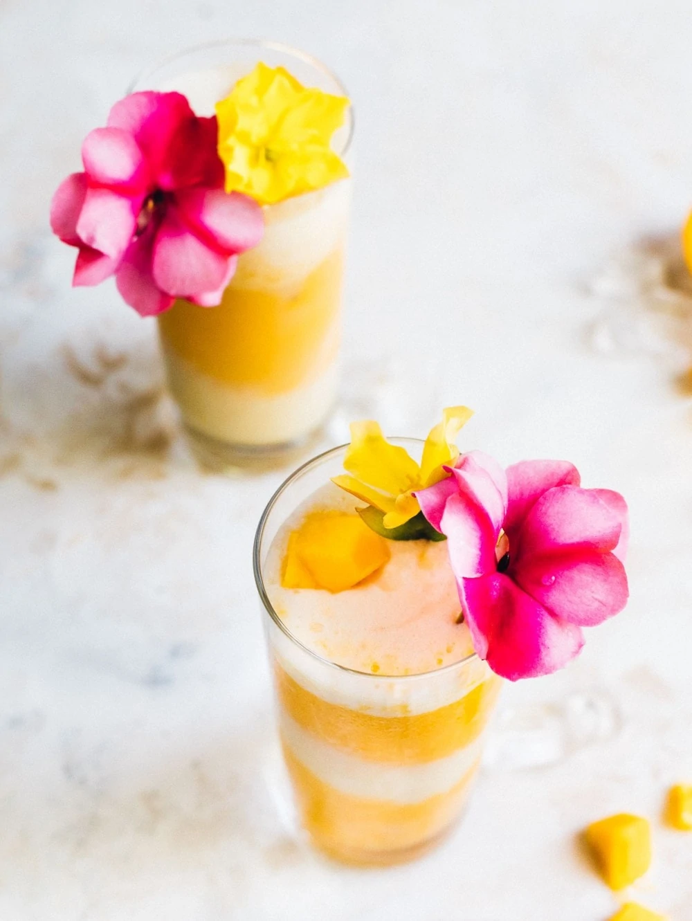 two mango and coconut cocktails with pink and yellow flowers