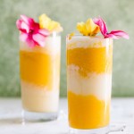 two mango and coconut cocktails with pink and yellow flowers