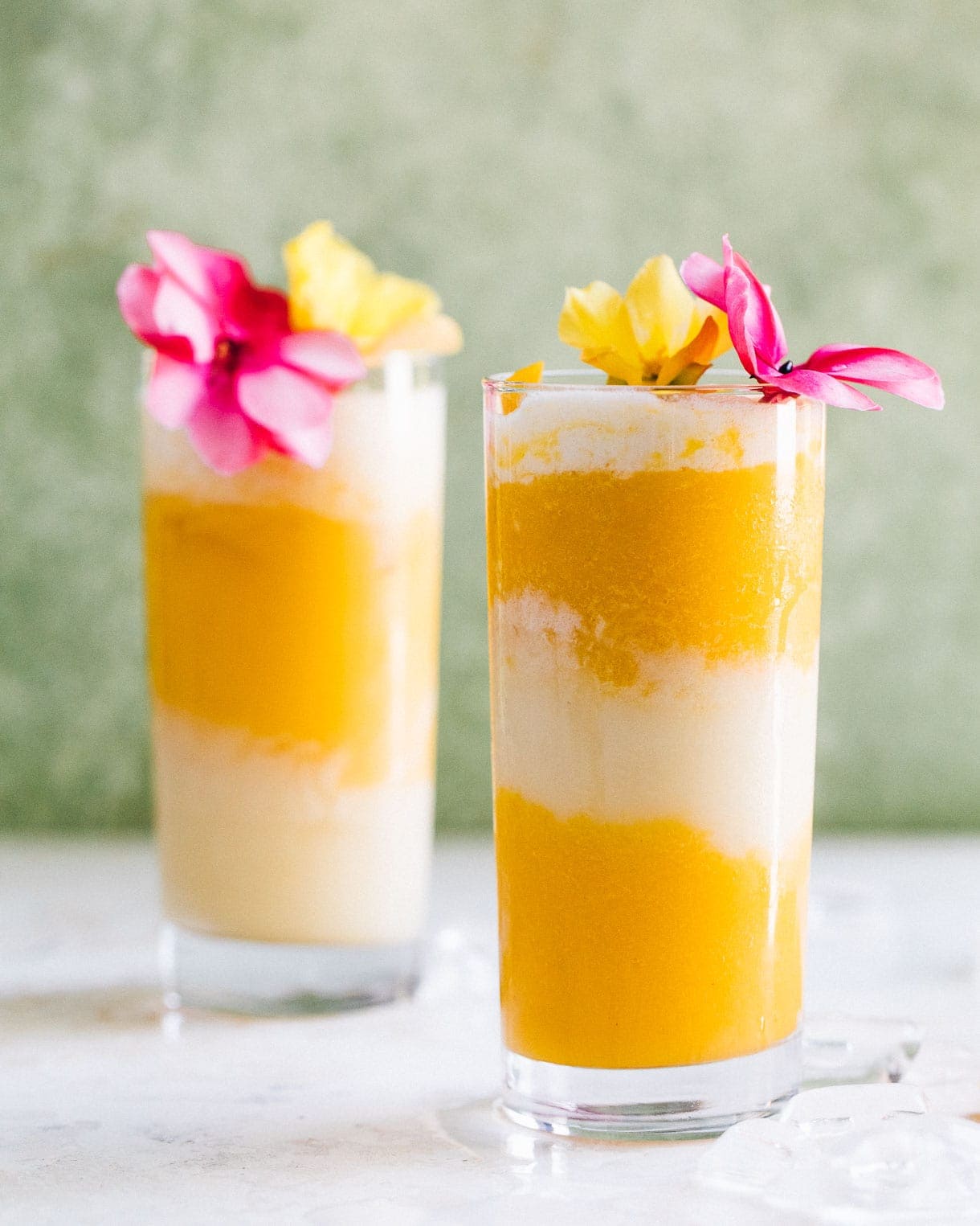 two mango and coconut cocktails with pink and yellow flowers