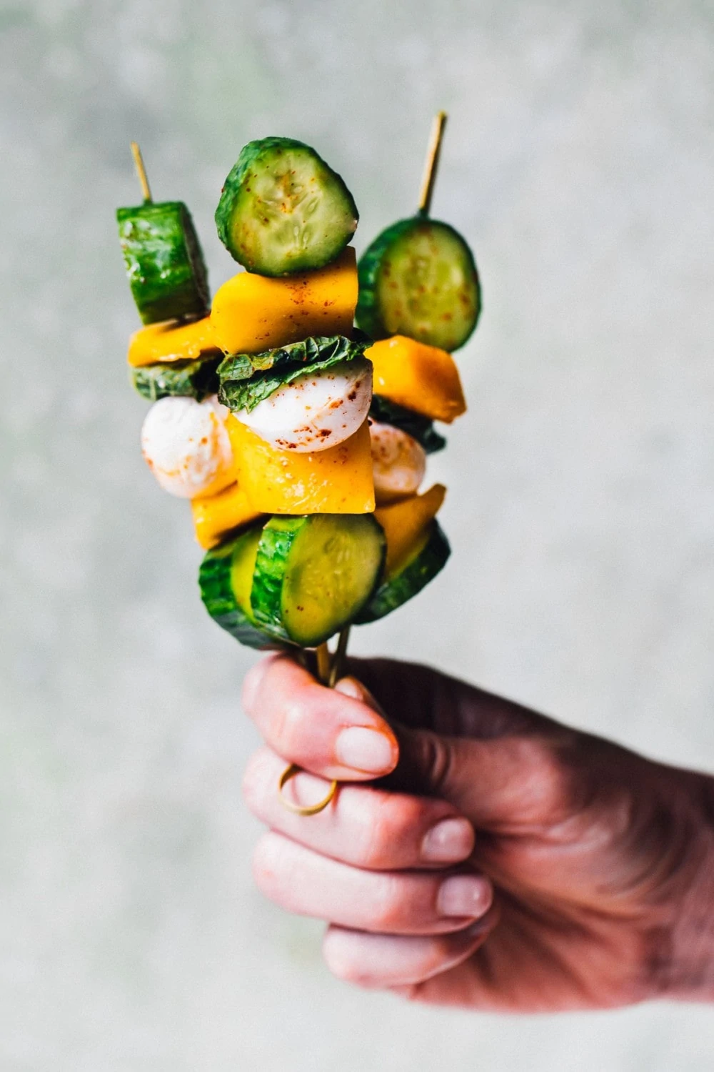 holding mango cucumber kabobs on a stick in one hand