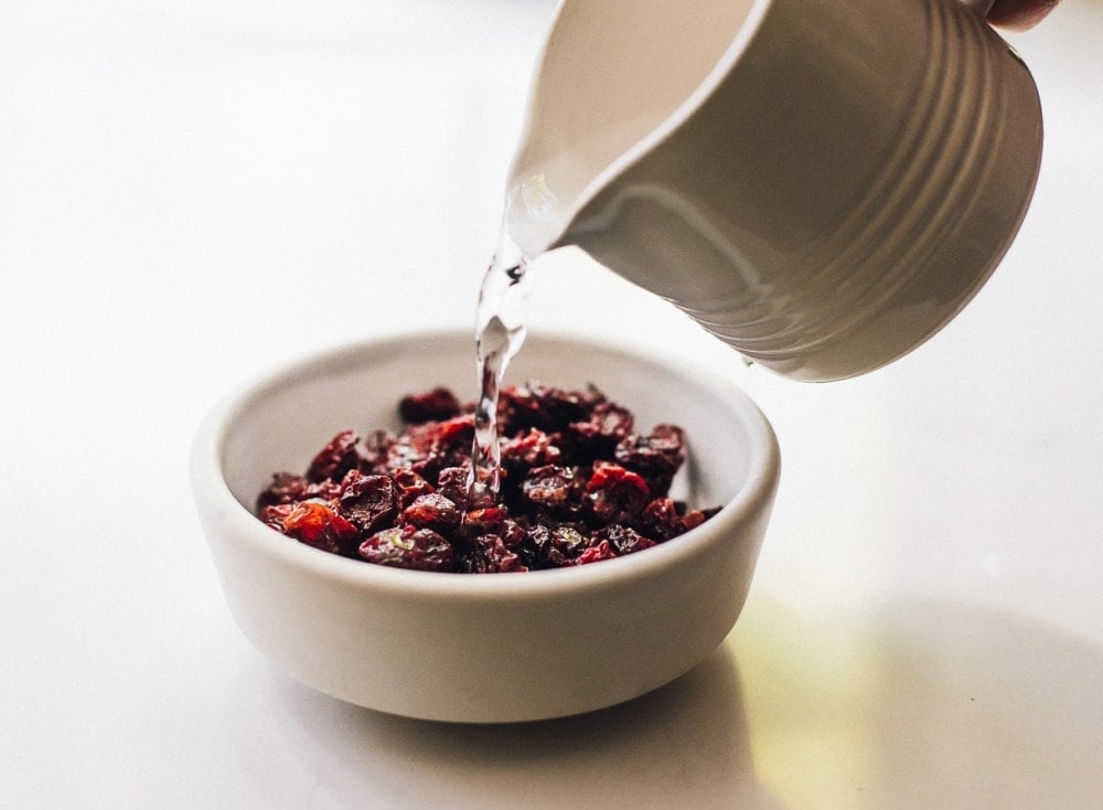 pouring hot water onto dried tart cherries in a white bowl