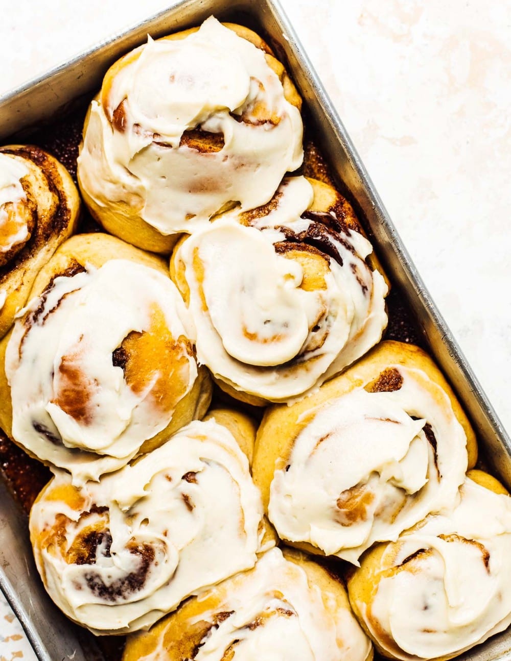 Sourdough Cinnamon Rolls, frosted with cream cheese frosting in an aluminum baking pan