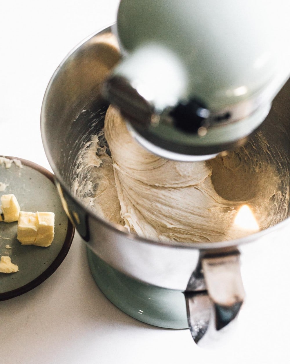 cinnamon roll dough being mixed in  a kitchenaid stand mixer, with butter on plate to its left