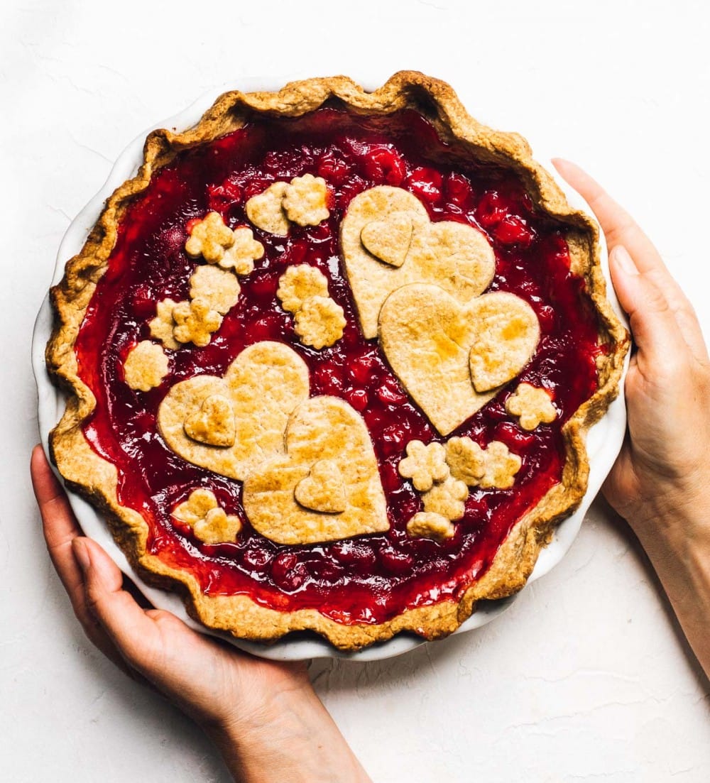 holding tart cherry pie in a white pie plate, with hearts decorated on top