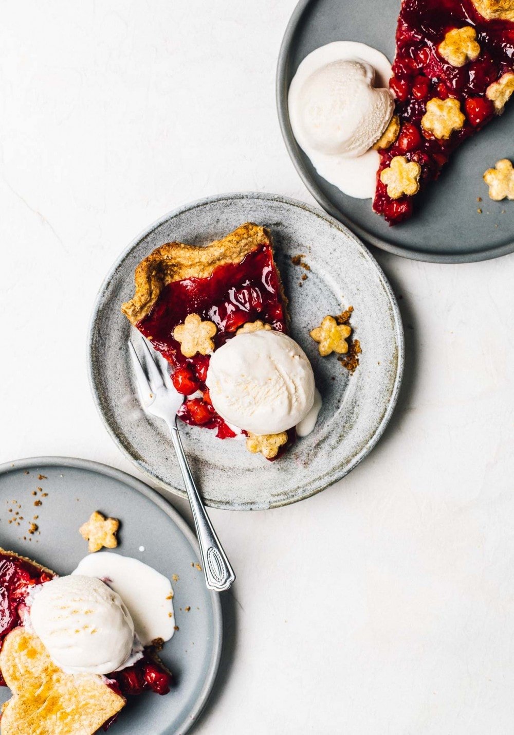 a slice of cherry pie with vanilla ice cream, on 3 plates, overhead photo