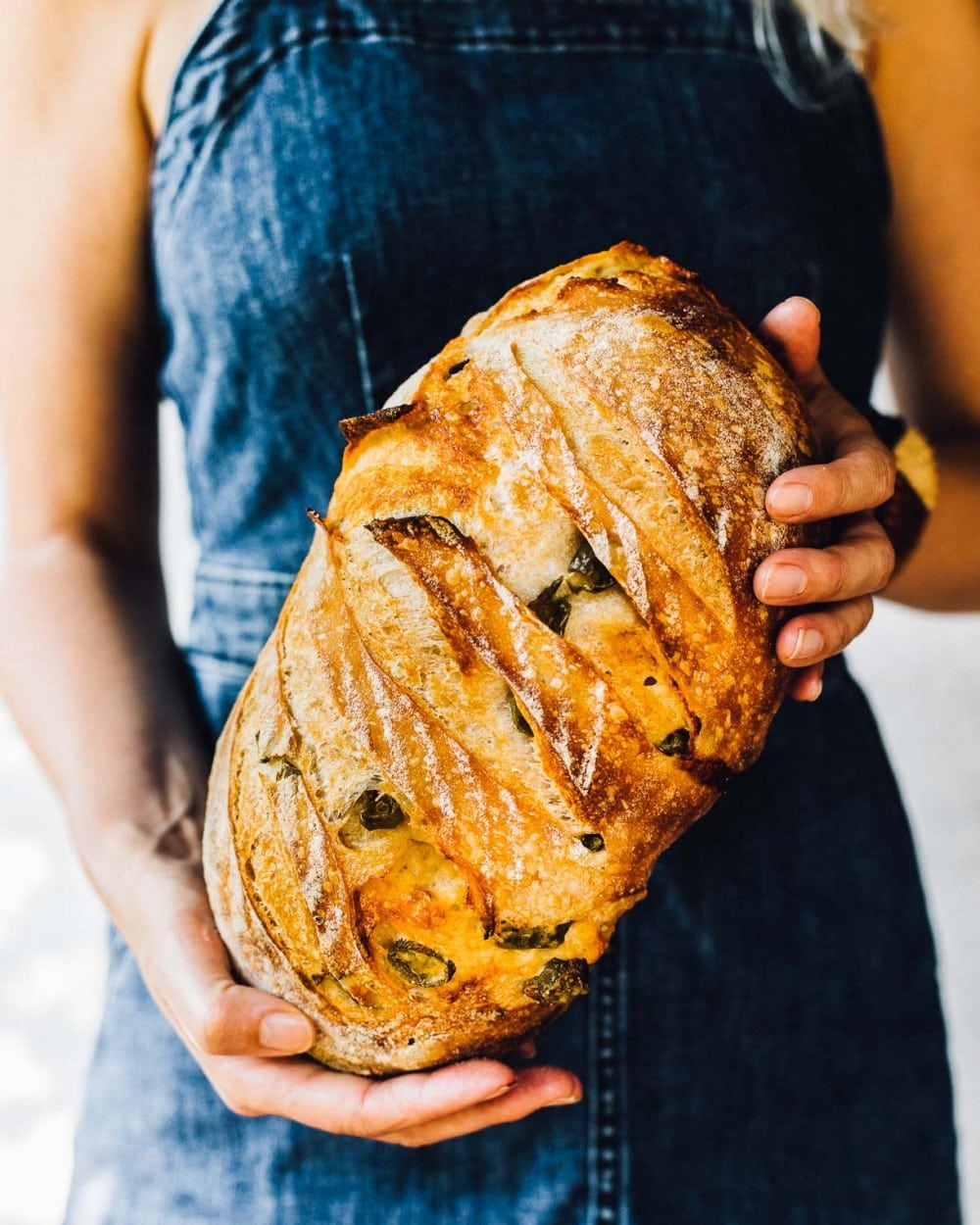 girl holding a loaf of sourdough bread with a denim dress on