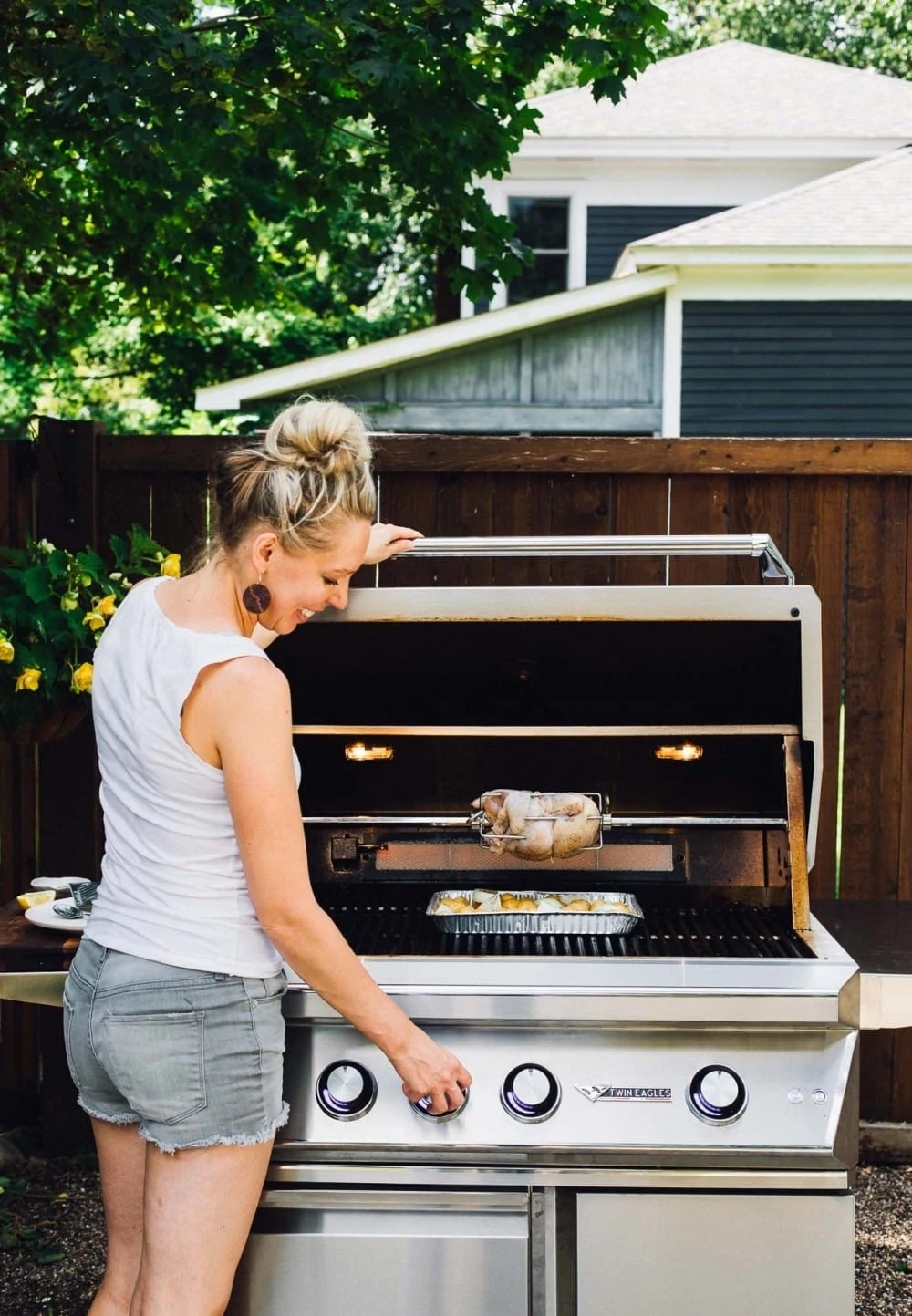 girl standing in front of a grill, with a chicken on a rotisserie
