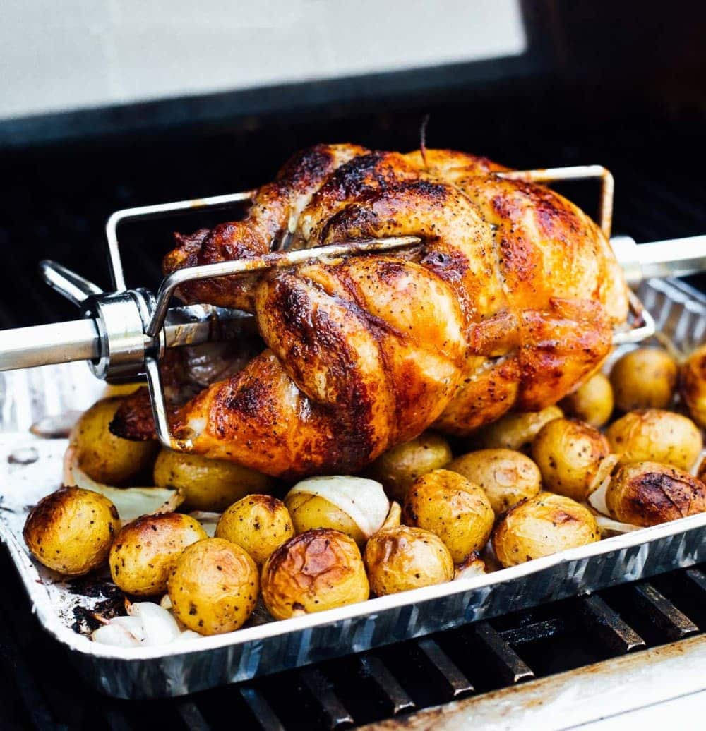 rotisserie chicken sitting on top of potatoes and onions in an aluminum pan