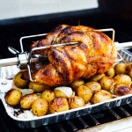rotisserie chicken sitting on top of potatoes and onions in an aluminum pan