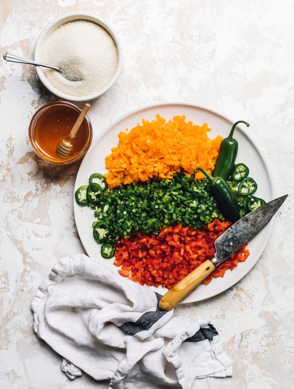 three types of bell peppers chopped and on plate. with jar of honey and bowl of sugar to its right. linen towards the bottom of photo.