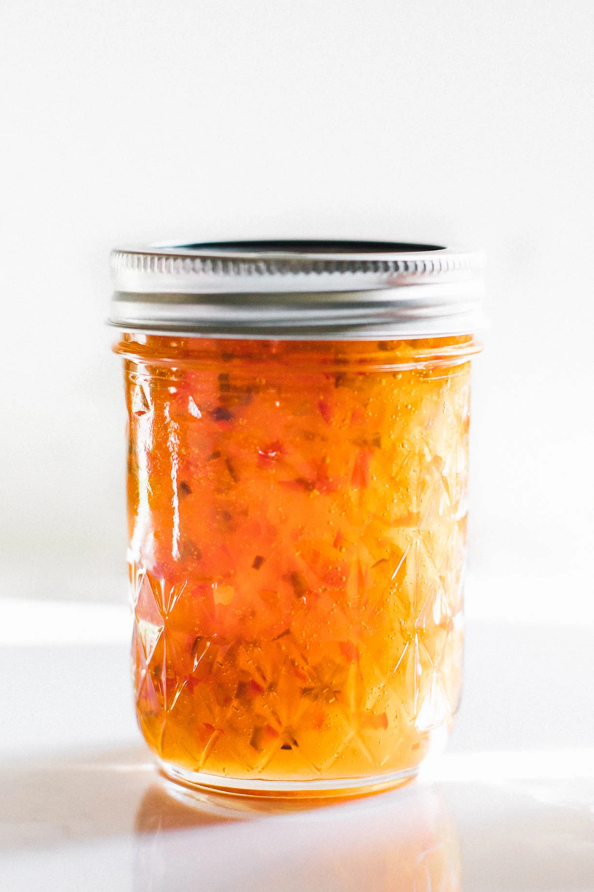clear jar with hot pepper jelly inside of it, stainless steel lid