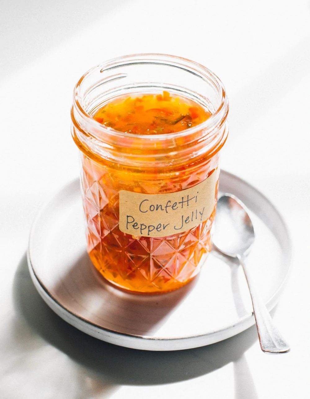 hot pepper jelly in a small glass canning jar with spoon to its right, both on a round plate