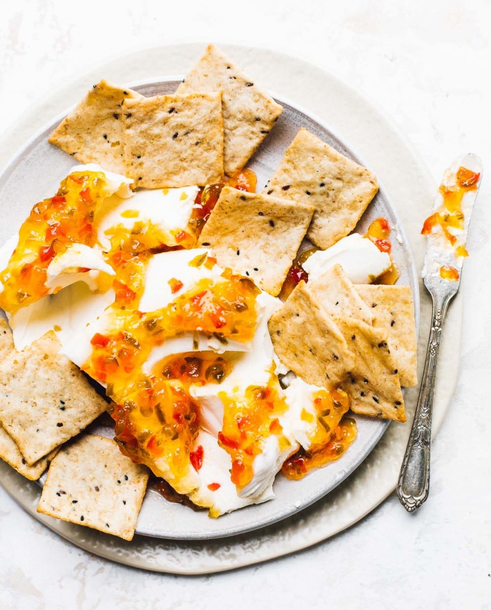 hot pepper jelly over a block of cream cheese with crackers surrounding it, knife to the right, on two stacked plates