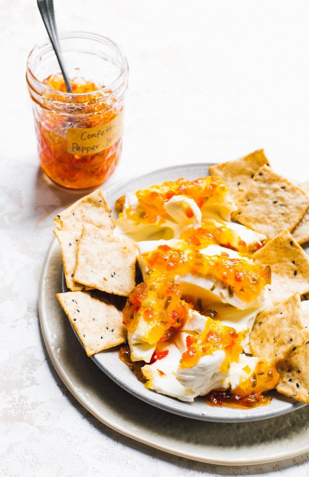 hot pepper jelly swirled into cream cheese, surrounded by crackers on a plate with the jar of pepper jelly in backround